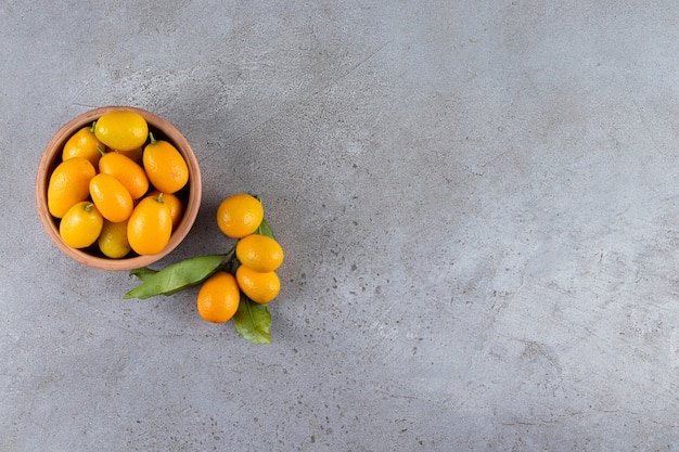 Fresh whole citrus cumquat fruits with leaves placed in wooden bowl