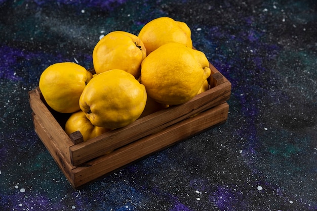 Fresh whole quince fruits in wooden box on dark table. 