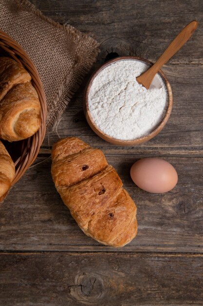 Freshly baked croissants with brown chicken egg and flour placed on a wooden table . High quality photo