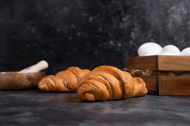 Freshly baked croissants with chicken eggs and wooden bowl of flour .