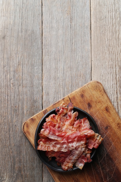 Fried bacon on black plate and wooden cutting board