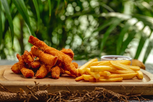 Fried breaded chicken breast strips with ketchup and french fries on a wooden board