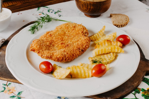 fried chicken along with potatoes red tomatoe inside white plate on brown desk