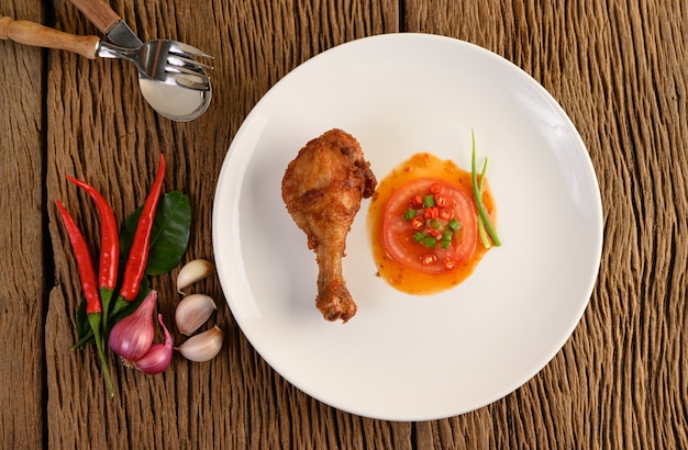 Fried chicken legs on a white plate with sauce and garlic, Shallot, chili.