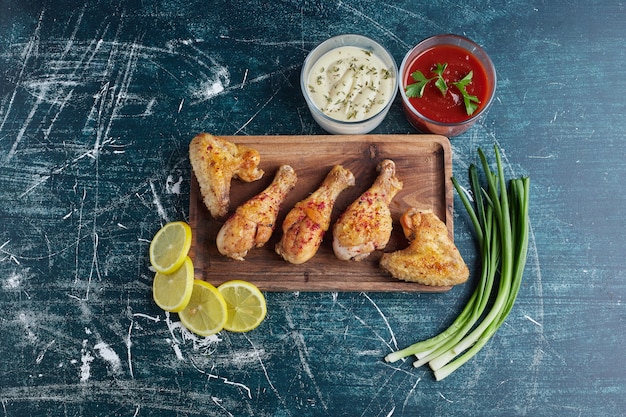 Free photo fried chicken legs with lemon and onion on a wooden board.