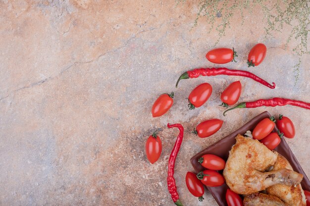 Fried chicken meat in a ceramic platter with chilies and cherry tomatoes.