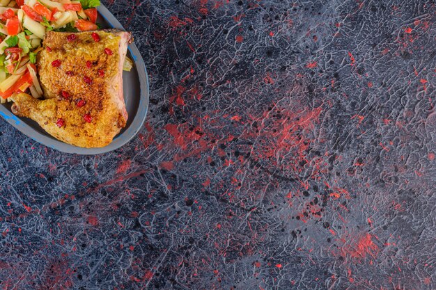 Fried chicken meat with mixed vegetable salad on a dark surface