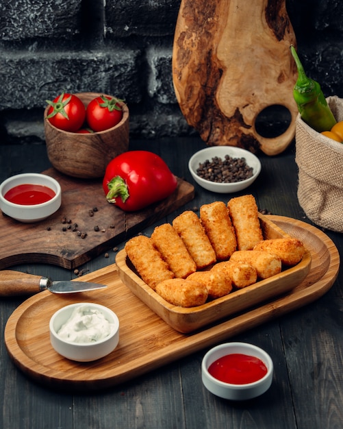 Free photo fried chicken sticks on a wooden board with mayonnaise and tomato sauce.