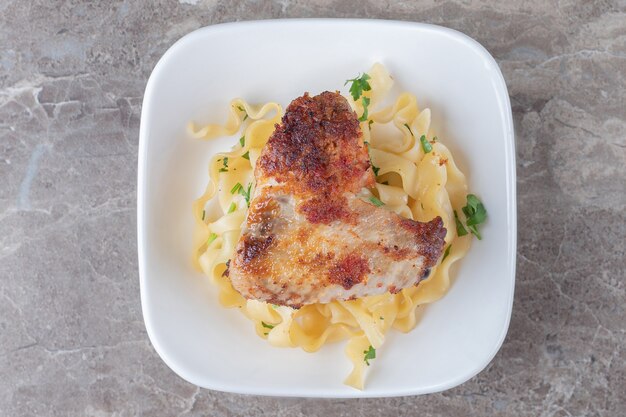 Fried chicken wingover spaghetti on the plate , on the marble.