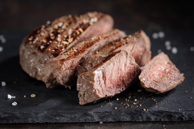 Fried cooked grilled meat with spices cut in slices served on dark slate Closeup