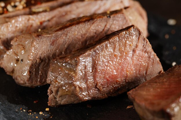 Fried cooked grilled meat with spices cut in slices served on dark slate Closeup