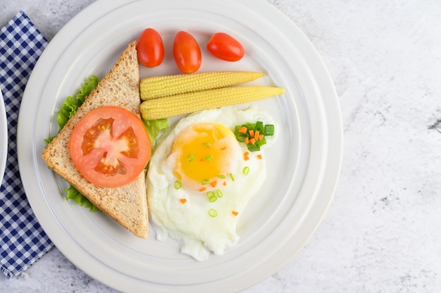 A fried egg laying on a toast, topped with pepper seeds with carrots, baby corn and spring onions.