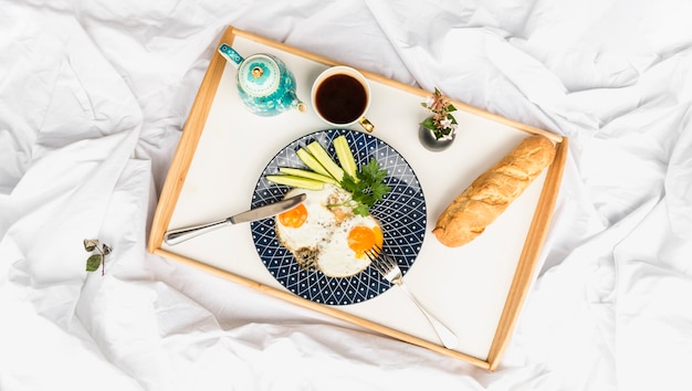 Free photo fried egg omelette with bread and tea on wooden tray over the bed