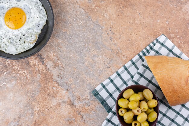 Fried egg in a pan served with green marinated olives