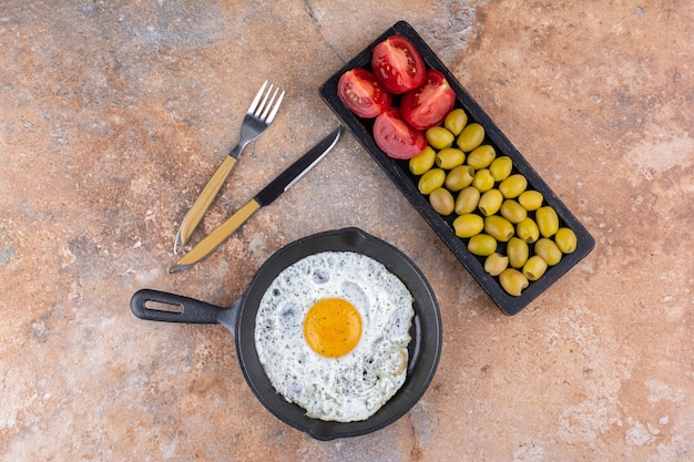 Free photo fried egg in a pan served with green marinated olives