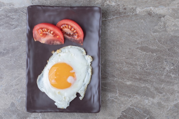 Fried egg and tomato slices on dark plate.