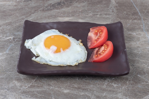 Free photo fried egg and tomato slices on dark plate.