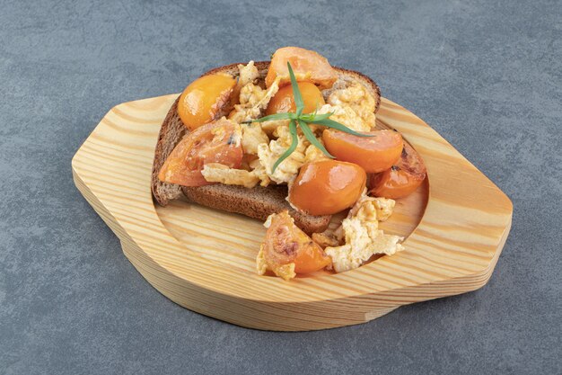 Fried egg, tomatoes and bread on wooden plate.