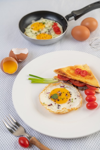 Fried egg on a white plate with toast, sliced ​​Spring onion and sliced ​​tomatoes