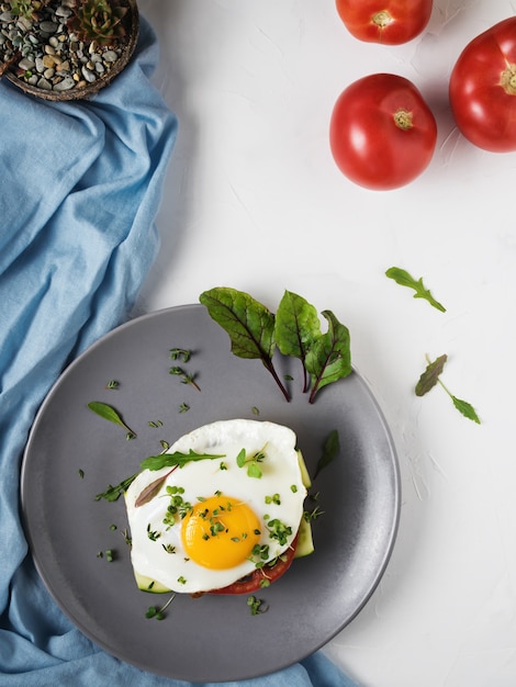 Free photo fried egg with tomatoes and leaves of arugula and thyme on bread in a gray plate