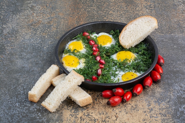 Free photo fried eggs with dill, pomegranate seeds and bread slices.