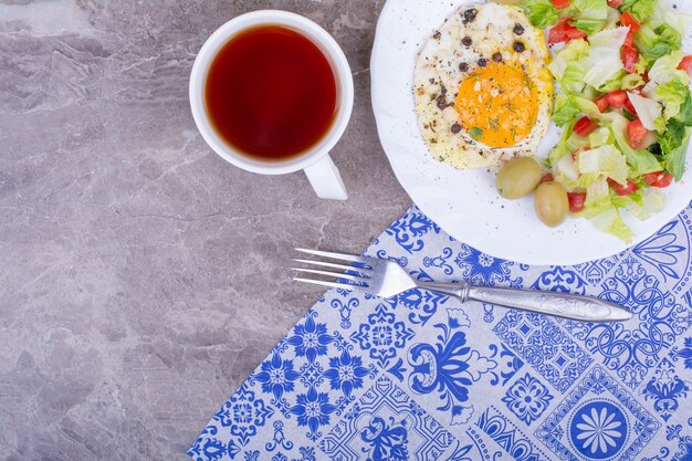 Free photo fried eggs with green salad and a cup of tea.