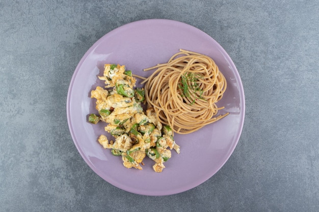 Fried eggs with spaghetti on purple plate.