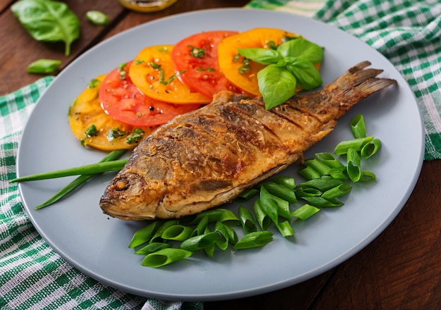 Fried fish carp and fresh vegetable salad on wooden table.