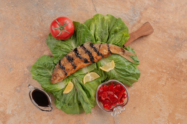 Free photo fried fish on lettuce with lemon slices, pickles and pomegranate sauce.