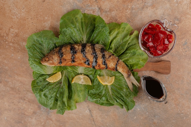 Free photo fried fish on lettuce with lemon slices, pickles and pomegranate sauce.