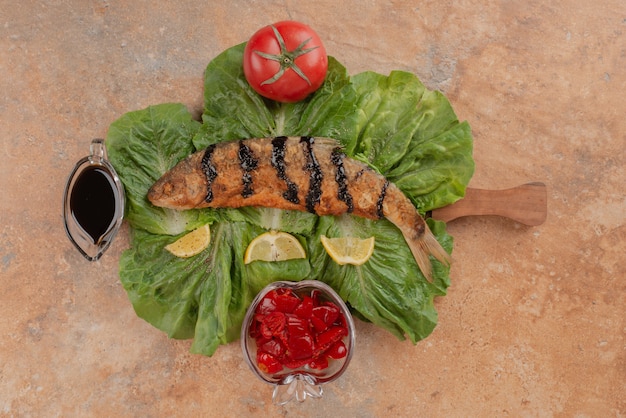 Fried fish on lettuce with lemon slices, pickles and pomegranate sauce.