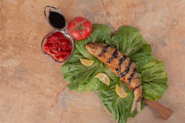 Fried fish on lettuce with lemon slices, pickles and pomegranate sauce.