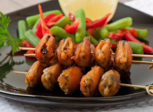 Fried mussels with onions on skewers c garnish of green beans and paprika