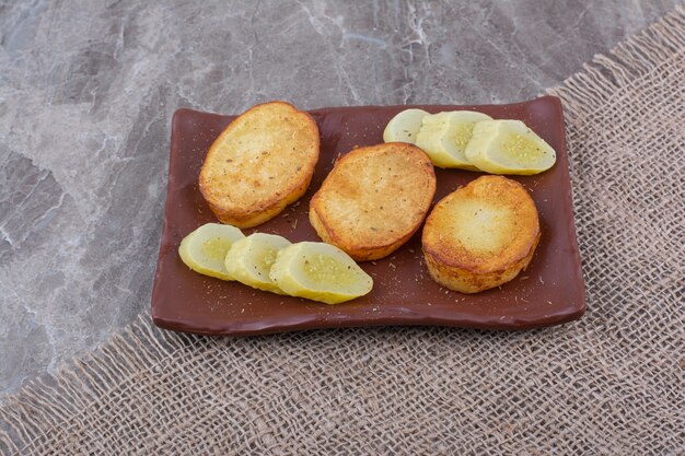 Fried potato slices and pickled cucumbers on plate.