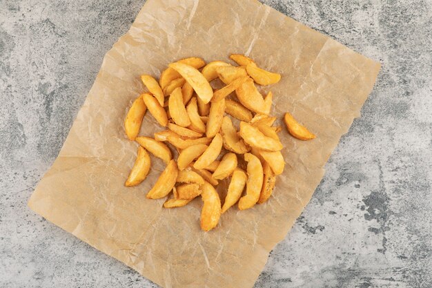 Fried potatoes on greaseproof paper on a stone background.