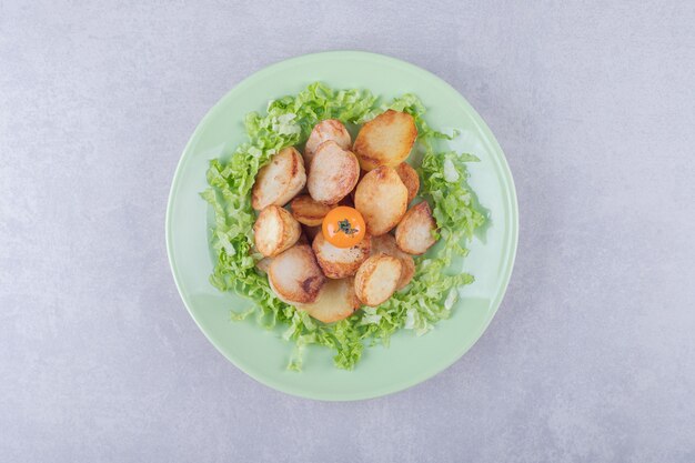 Fried potatoes and lettuce on green plate. 