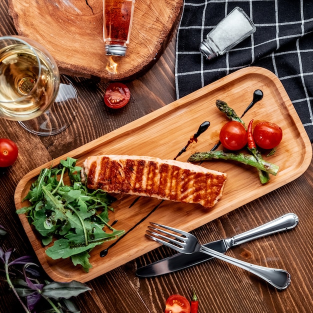 Fried salmon with vegetables on wooden board top view