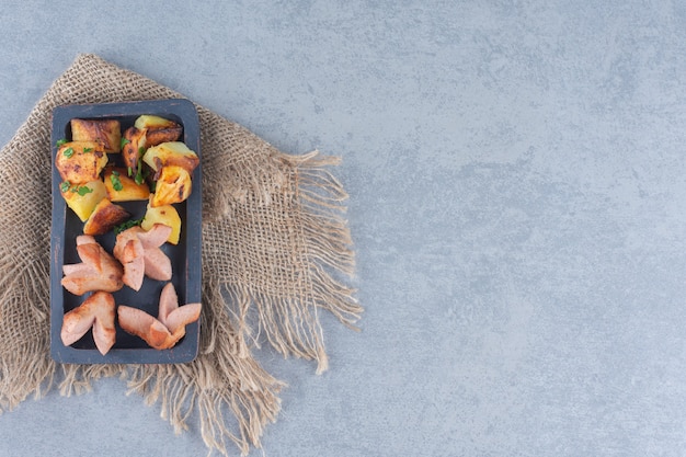 Fried sausage with potato on black wooden plate. 