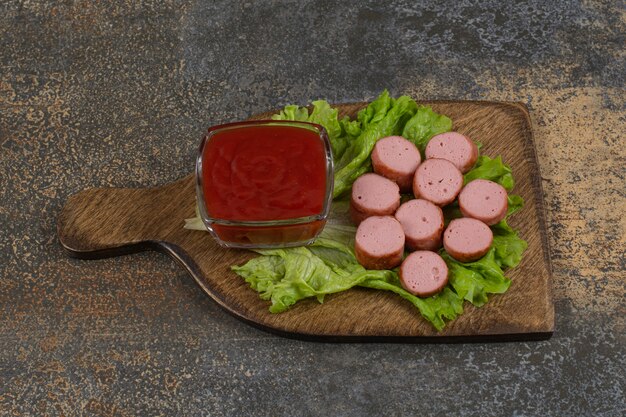 Fried sliced sausages and ketchup on wooden board.