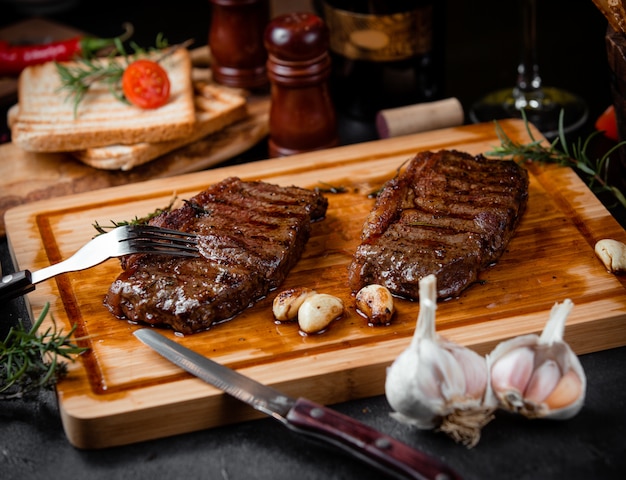 Fried steak pieces on a wooden board and garlic