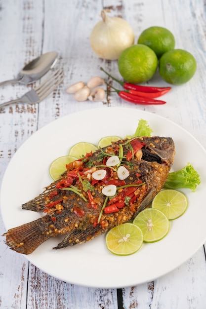 Fried tilapia with chili sauce,  lemon salad and garlic on a plate on a white wooden table.