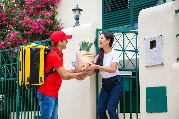 Friendly food courier with isothermal backpack giving package from grocery store to customer. Shipping or delivery service concept