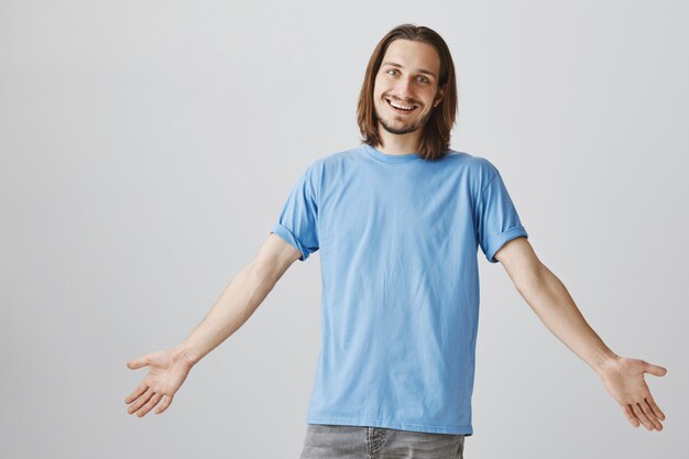 Friendly happy hipster guy spread hands, welcome guests and smiling