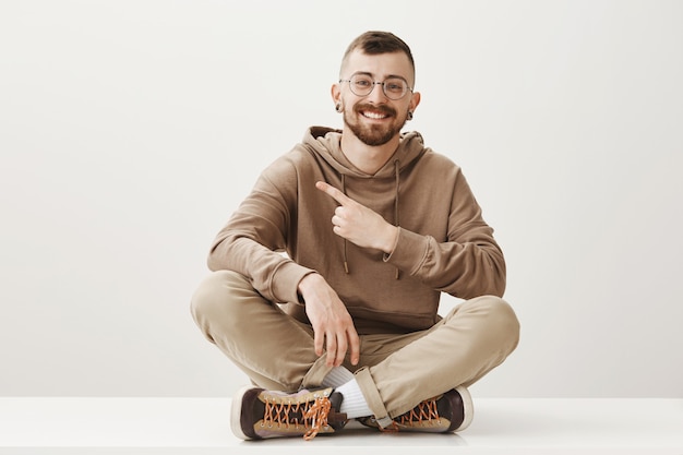 Friendly happy man sit on floor and pointing finger upper left corner, showing way