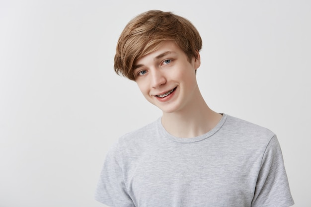 Friendly looking positive fair-haired young stylish man with blue eyes smiling broadly dressed casually, rejoicing his life, standing . Youth, positive emotions and feelings