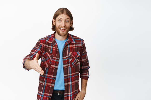 Friendly smiling man stretch out hand for handshake standing in shirt against white background