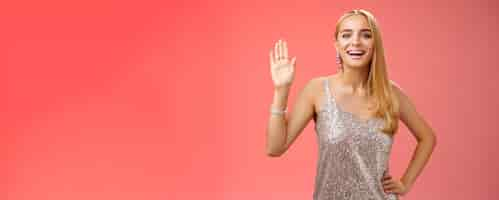 Free photo friendly stylish glamour attractive blond caucasian woman in silver glittering dress hold hand waist waiving palm hello hi what up gesture smiling introducing herself party boyfriend friend