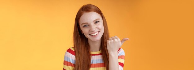 Friendly tender feminine kind redhead woman blue eyes pointing thumb left showing location where fin