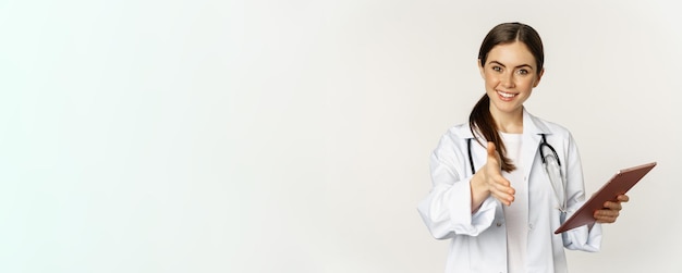 Free photo friendly young female doctor physician stretch out hand for handshake greeting patient in clinic hol