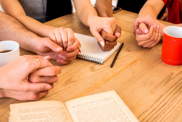 Free photo friends holding hands near stationery and coffee cups over wooden desk